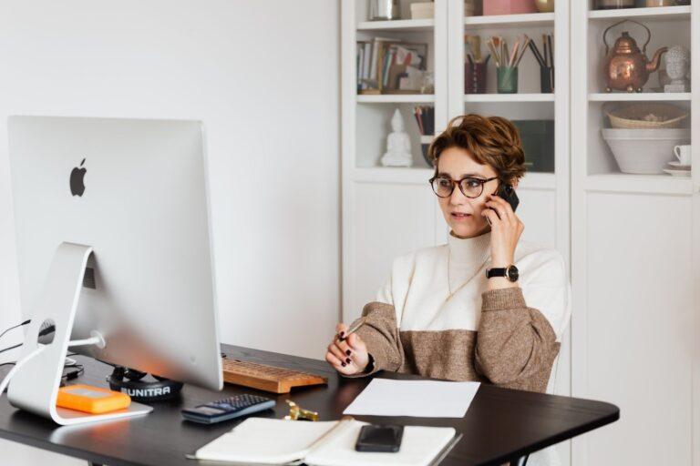 Zo houd je grip op je cijfers en creëer je rust in je onderneming Smart confident female managing director listening to employees report on smartphone while working on computer in light modern office